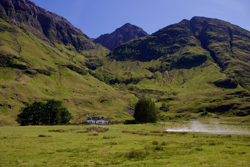 A white cottage on the green floor of Glencoe, beneath the mountains of the glen