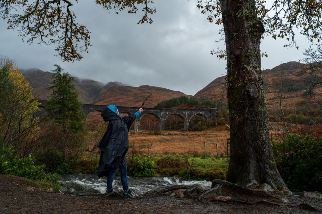 A visitor in a raincoat looking out at the Glenfinnan Viaduct from the trail