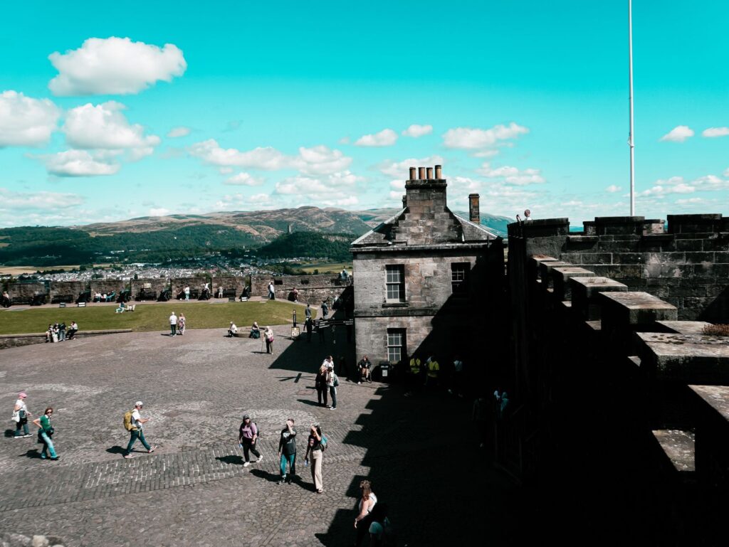 Visitors exploring the grounds of Stirling Castle on a sunny day, with the walls and hills beyond